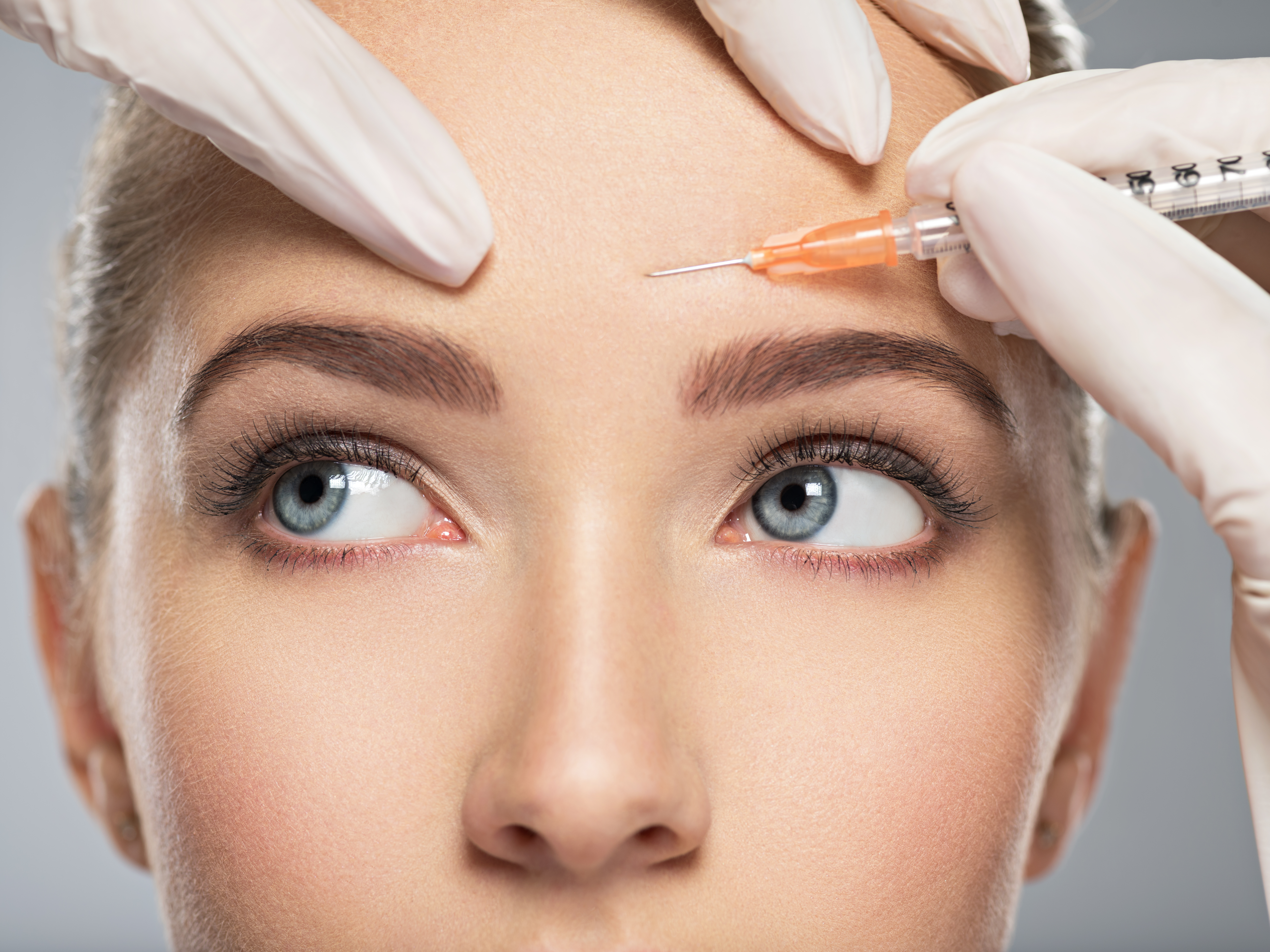 A closeup of a woman getting a botox injection in her forehead